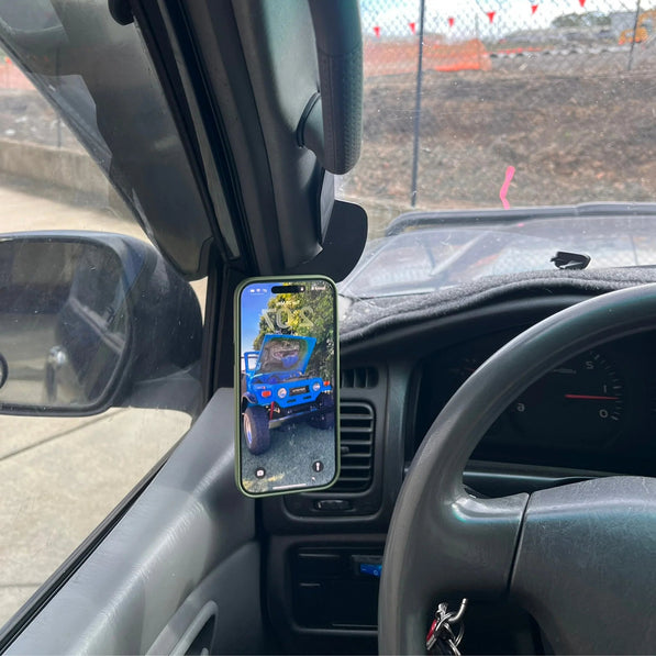 Phone mounted on a car dashboard displaying an image of a blue truck, with a view of a construction site outside.