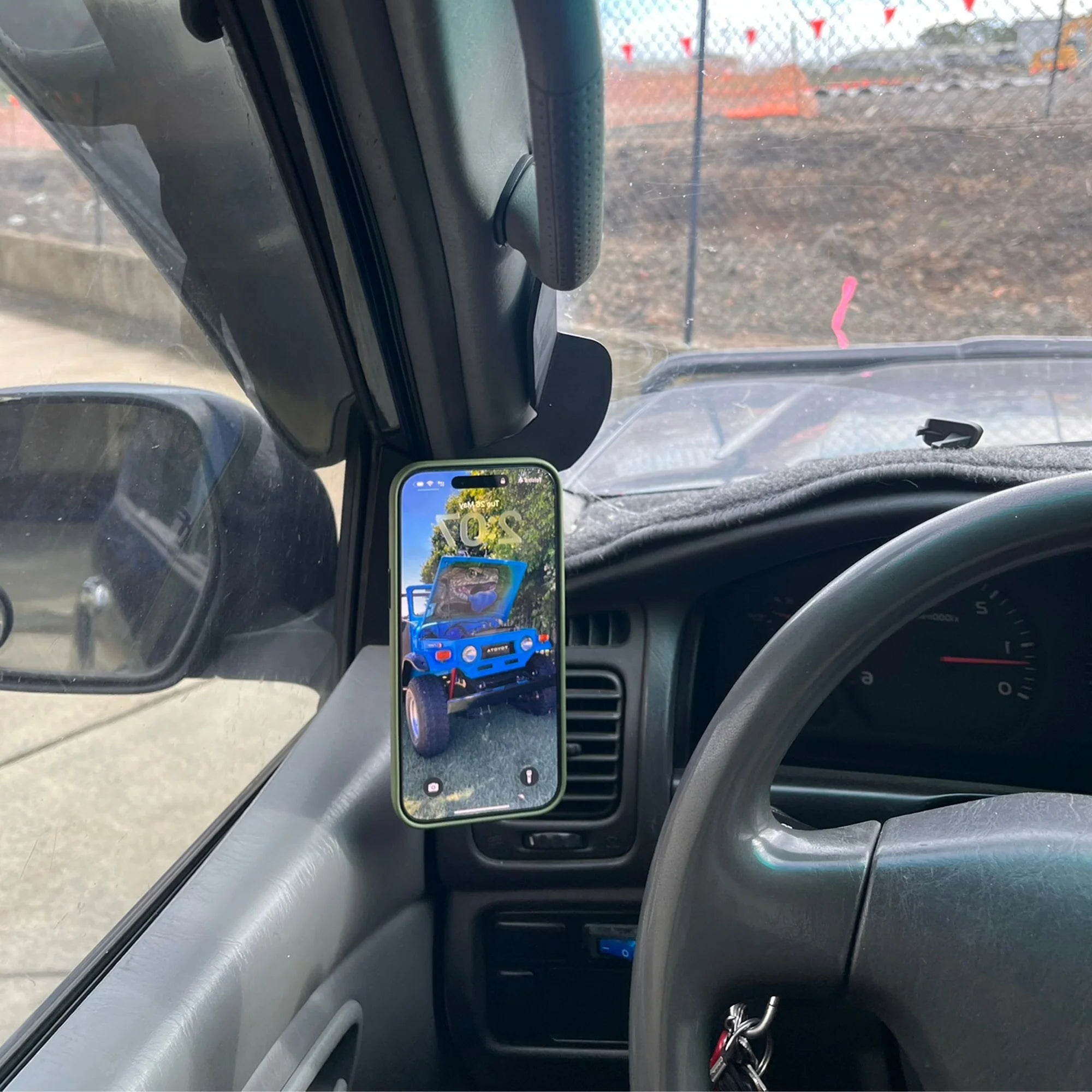 Phone mounted on a car dashboard displaying an image of a blue truck, with a view of a construction site outside.
